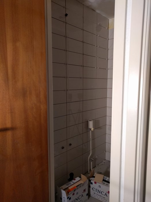 Nyansskillnad på nyinköpta kakelplattor jämfört med befintliga på en badrumsvägg under renovering.