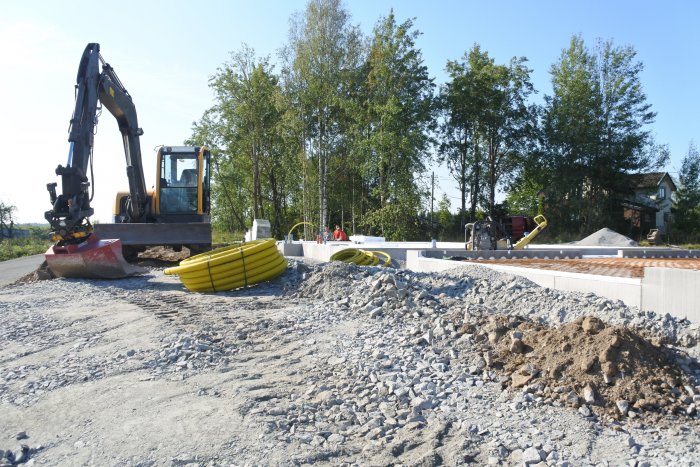 Tomt med grävmaskin och förberedelser för gjutning av garage, inklusive avloppsrör och cellplastisolering.