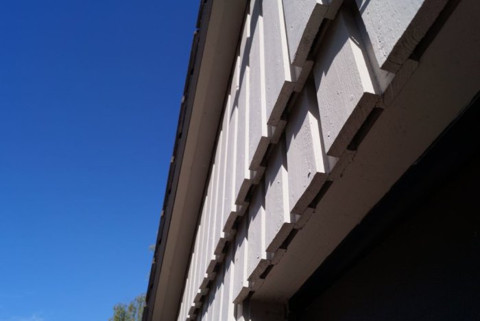 Perspektivvy av fasadpanel med nysågad droppnäsa under ett tydligt överhäng, mot en klarblå himmel.