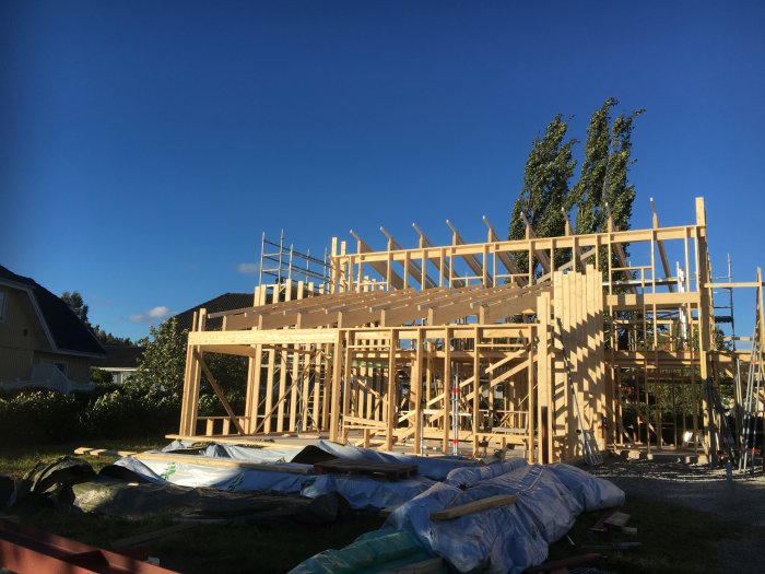 Byggställningar och trästrukturer för ett hus och carport under klar himmel.