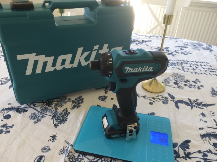 Makita skruvdragare på våg med viktvisning 986g, bredvid plastväskan med Makita-logotyp.