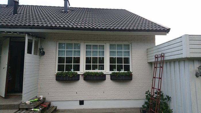 Husfasad med vita fönster och spröjs fastsatta, blomlådor och en röd stege på verandan.