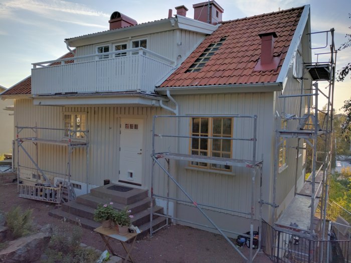 Renoveringsarbete på ett beige hus med spröjsade fönster och ställningar runtomkring.