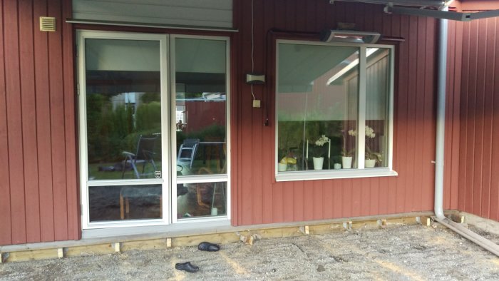 Husvägg med nedmonterad altan och synliga fundament inför en utbyggnad.