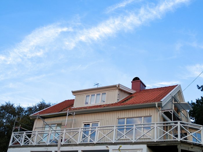 Fasad från 1938 på en äldre villa utan spröjsade fönster, med röd tegeltak och ställning framför.