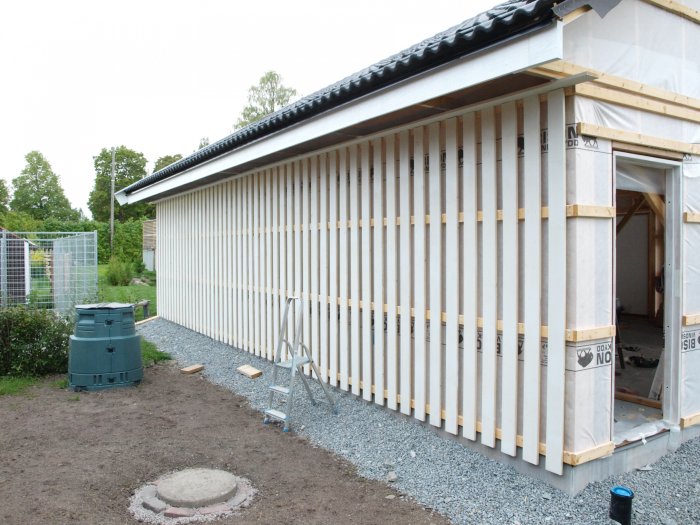 Ett hus under konstruktion med ofärdiga träpaneler och en stege till vänster.