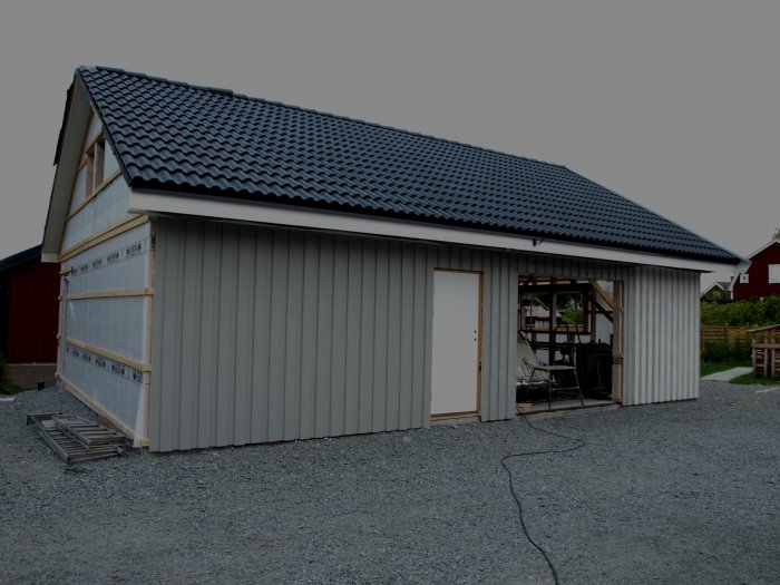 Nybyggd garagebyggnad med halvfärdig panel och målararbeten pågår.