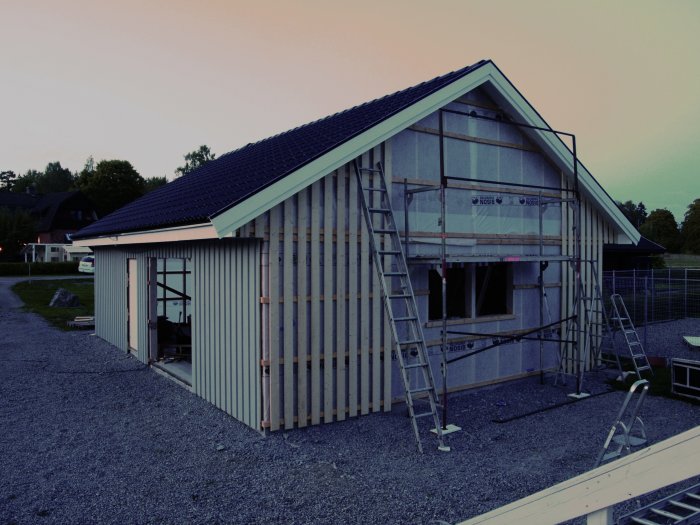 Hus under konstruktion med uppsatta panelspik, fasadisolering, och stegar längs väggen.
