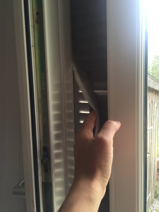 Hand som drar i ett smutsigt ventilationsfilter på sidan av ett fönster, visar att byta filter.