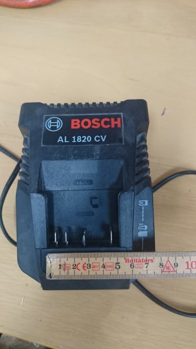 Bosch batteriladdare AL 1820 CV på ett arbetsbord med ett måttband framför.