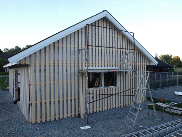 En trästomme till ett hus under konstruktion med synligt regelverk och en stege vid sidan.