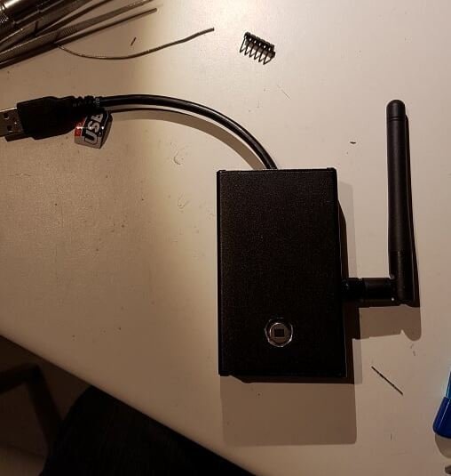 Ett svart aluminiumlåda för elektronikprojekt med en antenn, USB-kabel och lösa komponenter på ett bord.