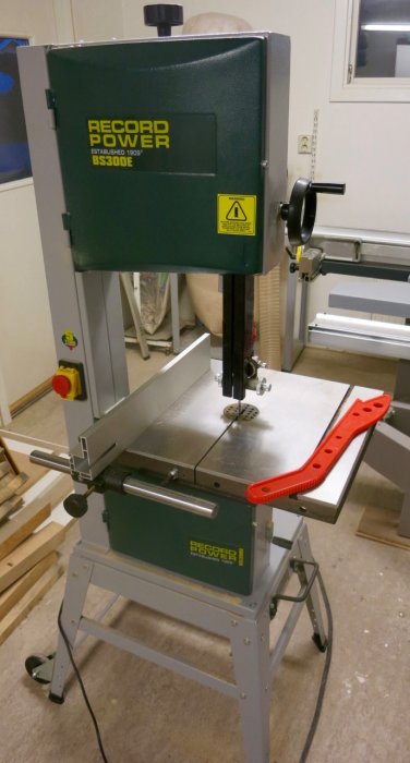 Bandsåg modell Record Power BS300E på ett grått metallställ i en verkstadsmiljö med svart sågblad och röd mitre-anhåll.