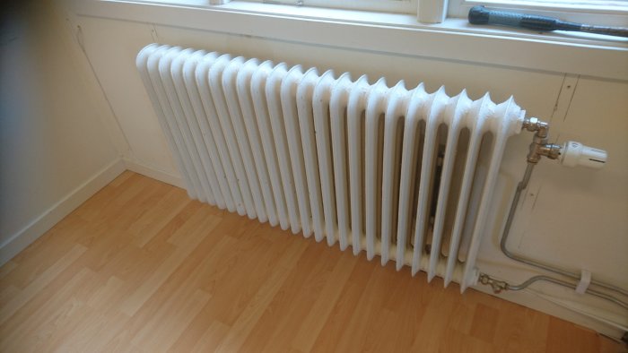 Vit sektionsradiator med termostat i ett rum, synliga rostfläckar undertill.