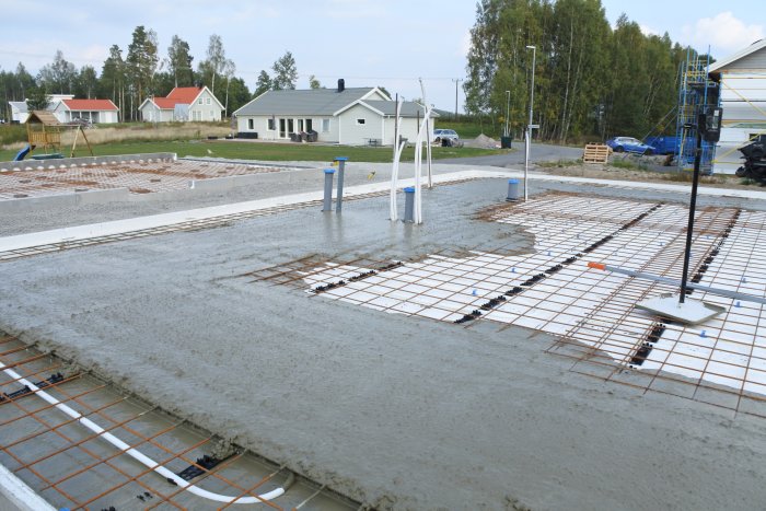 Nyligen gjuten betongplatta med armeringsjärn och synliga grundpelare, omgiven av husbyggen.