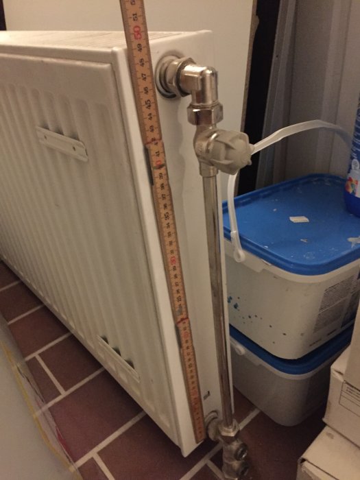 Mätning av radiatorhöjd med tumstock bredvid en radiator med ett kopplat termostatventil.