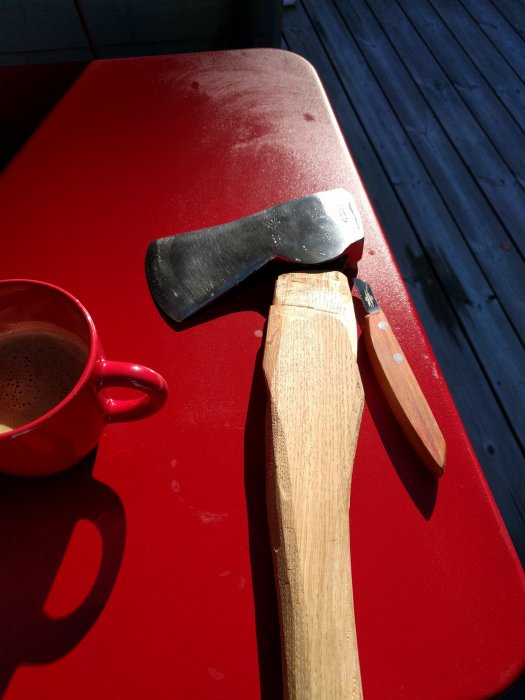 Yxhuvud på rött bord med obearbetat skaft och Hock-kniv, bredvid en kopp kaffe.