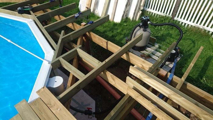 Träreglar och byggmaterial runt en pool under konstruktion, med verktyg och klämmor.