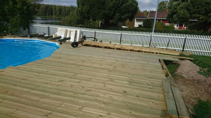 Nybyggd trätrall vid en pool med omonterade plankor och arbetsmaterial.