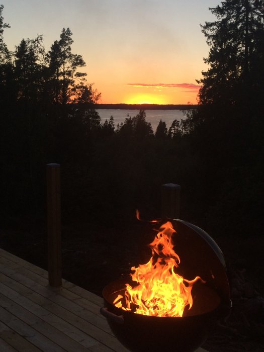 Solnedgång över vatten sedd från terrass med brinnande eldkorg i förgrunden.