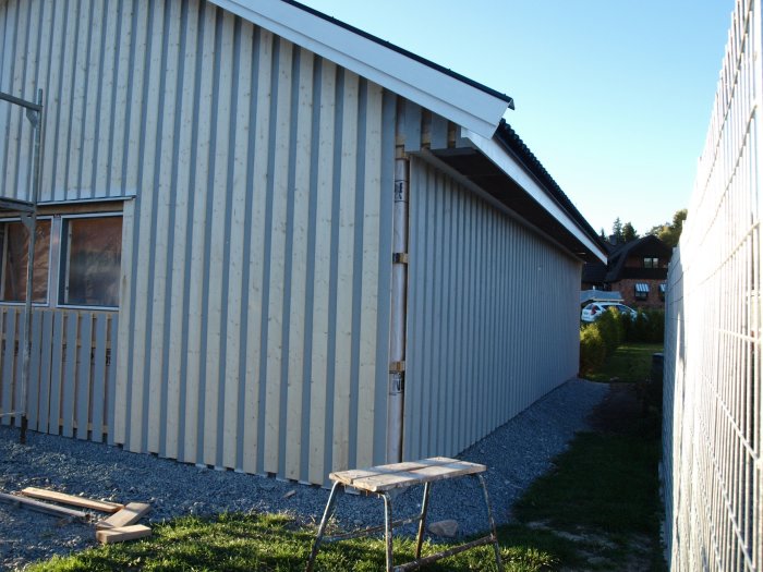 Färdigmonterad ljus träpanel på byggnad med synlig port och byggmaterial på marken.