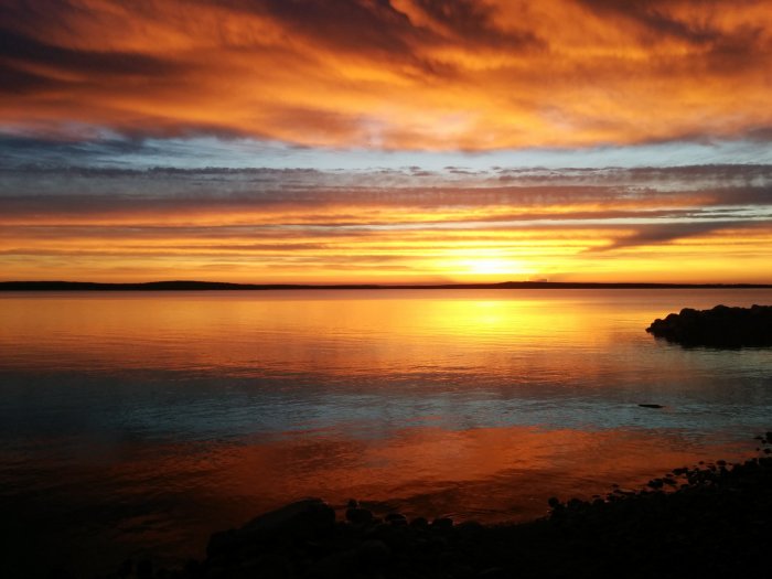 Solnedgång med intensiva orange färger i himlen reflekterade i vattnet vid Skellefteå.