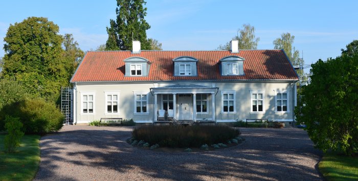 Ny målning på klassiskt hus med röd tegeltak, vit fasad och stegar på gaveln för pågående arbete.