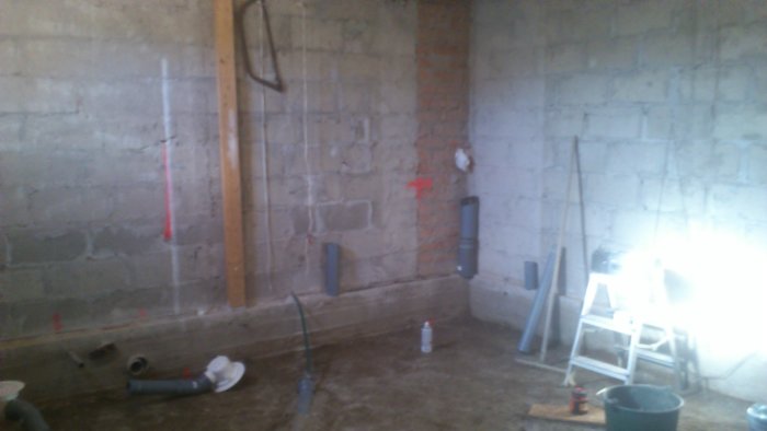 Otomfärdig källare med betongväggar, installationsrör och arbetsmaterial före golvgjutning.