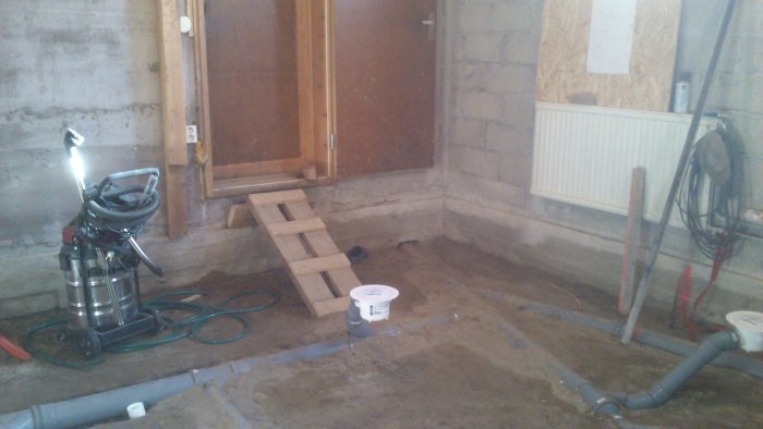 Källargolv under förberedelse för gjutning med synligt dräneringssystem och en byggdammsugare.