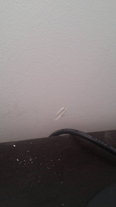 Vit betongvägg med en liten, tydlig skada och en kabel framför väggen.