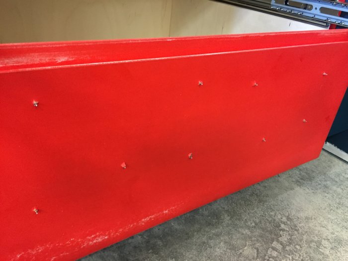 Röd möbeldel med synliga spikdyckertar efter renovering.