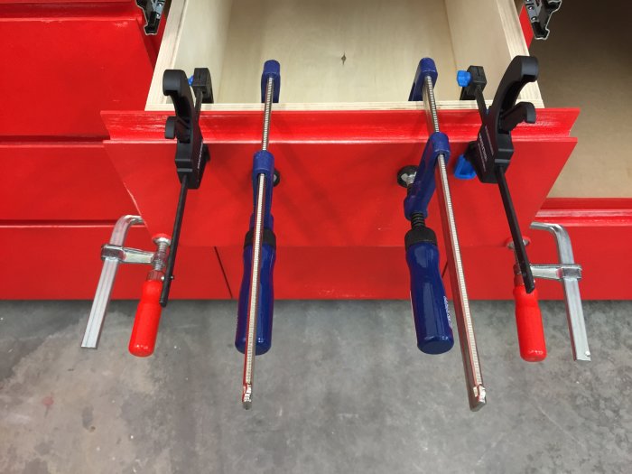 Skruvstäd och verktyg används på en träskiva och röd möbel.