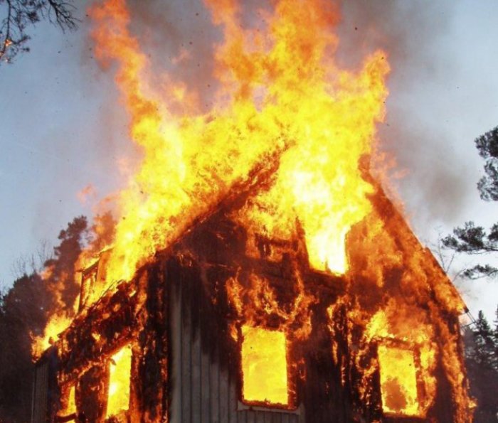 Brinnande trähus med intensiva lågor som slår ut genom fönster och tak.