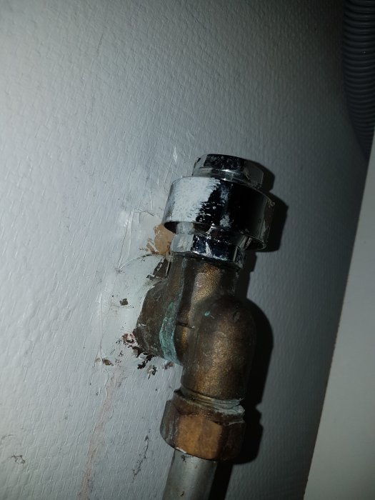 Vattenrörskoppling med läckage vid vägg, tätningsförsök synligt under hattliknande del.