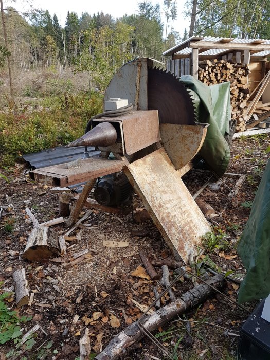 Gammal vedkap/klyv i utomhusmiljö med skogsbackgrund, synlig sågklinga och vedspillning.