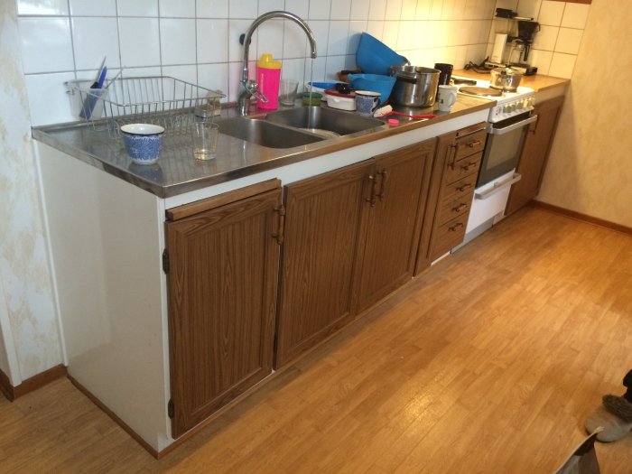 Ett kök med fulla diskbänkar och befintliga skåp där en diskmaskin ska installeras.