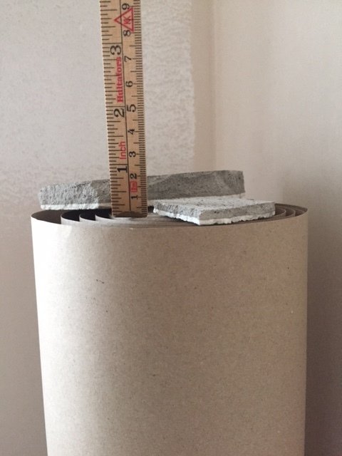 Tumstock mäter tjocklek på avslagen betongbit som ligger ovanpå en pappersrulle.