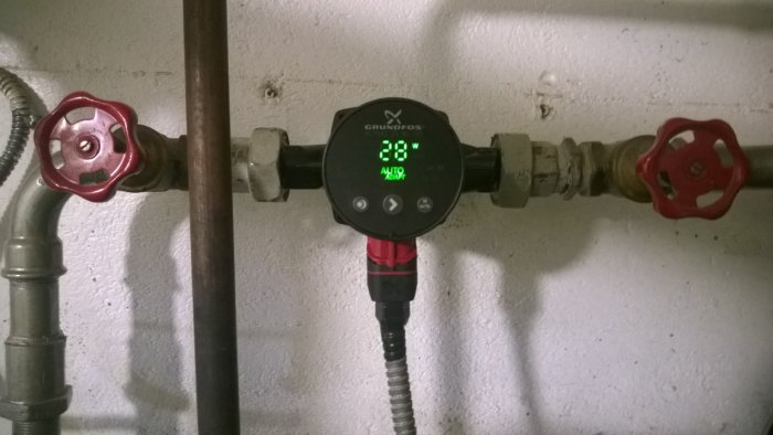 Nyinstallerad Grundfos cirkulationspump i ett pannrum med digital display och röda ventiler.