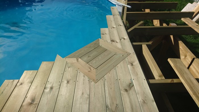 Trätrall omkring pool med ett öppet rektangulärt hål täckt av två trallbrädor bredvid en poolstädare.