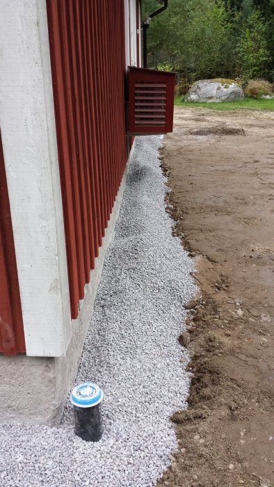 Grushög längs husvägg, över kantlisten där byggfog applicerats, med tom byggfogen-tub i förgrunden.