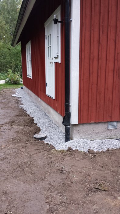 Fördelningsbrunn nära ytterdörren på hus med grus och omgrävd jord, hindrar större entréverandas byggnation.