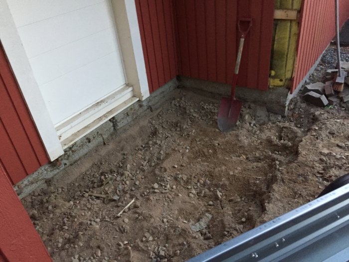 Nygrävd grop vid husvägg med spade som tecken på starten för renoveringsprojekt.