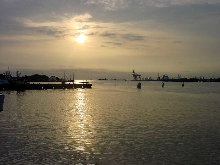 Solnedgång över en hamn med reflektioner på vattnet, hamnkranar i bakgrunden, tio år gammalt foto.