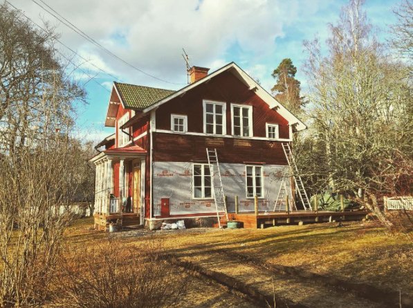 Renovering pågår av ett tvåvånings rött hus med vit snickeri, stegar lutade mot fasaden.