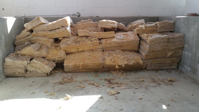 Stapel av gul fiberglasisolering som ligger i ett garage, med tecken på förvaring utomhus.