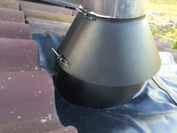 Nyinstallerad skorstenkrage med gummiduk och plastkragar på ett tegeltak.