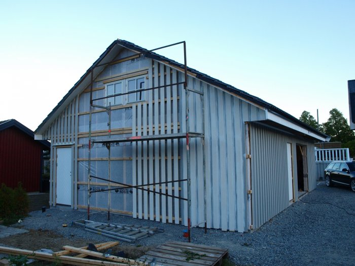 En delvis färdigmålad byggnad med regelverk synligt och uppsatta byggställningar vid ena gaveln.
