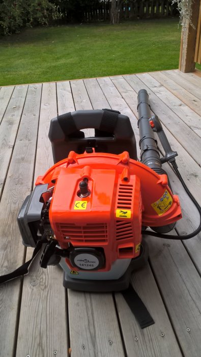 Ryggburen orange VidaXL maskin med blåsrör, tank och sele på en träaltan med gräsmatta i bakgrunden.