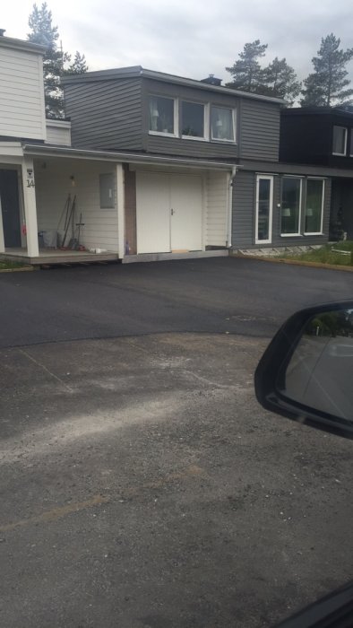 Asfalterad uppfart framför hus med ombyggt garage till förråd med vit panel där garagedörrar varit.