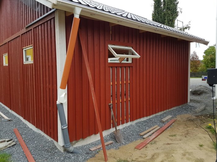 Rödfärgad husvägg med synlig stolpe mellan garageportar, väntar på invändigt arbete och ytterligare elektriska uttag.